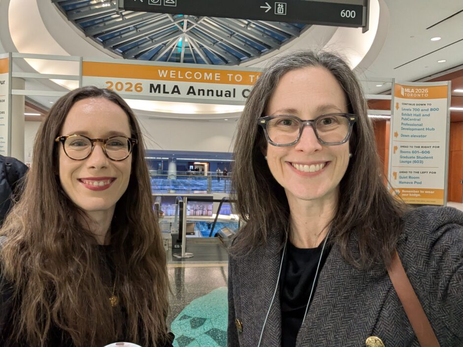 Two women stand smiling in front of the 2026 MLA Convention banner
