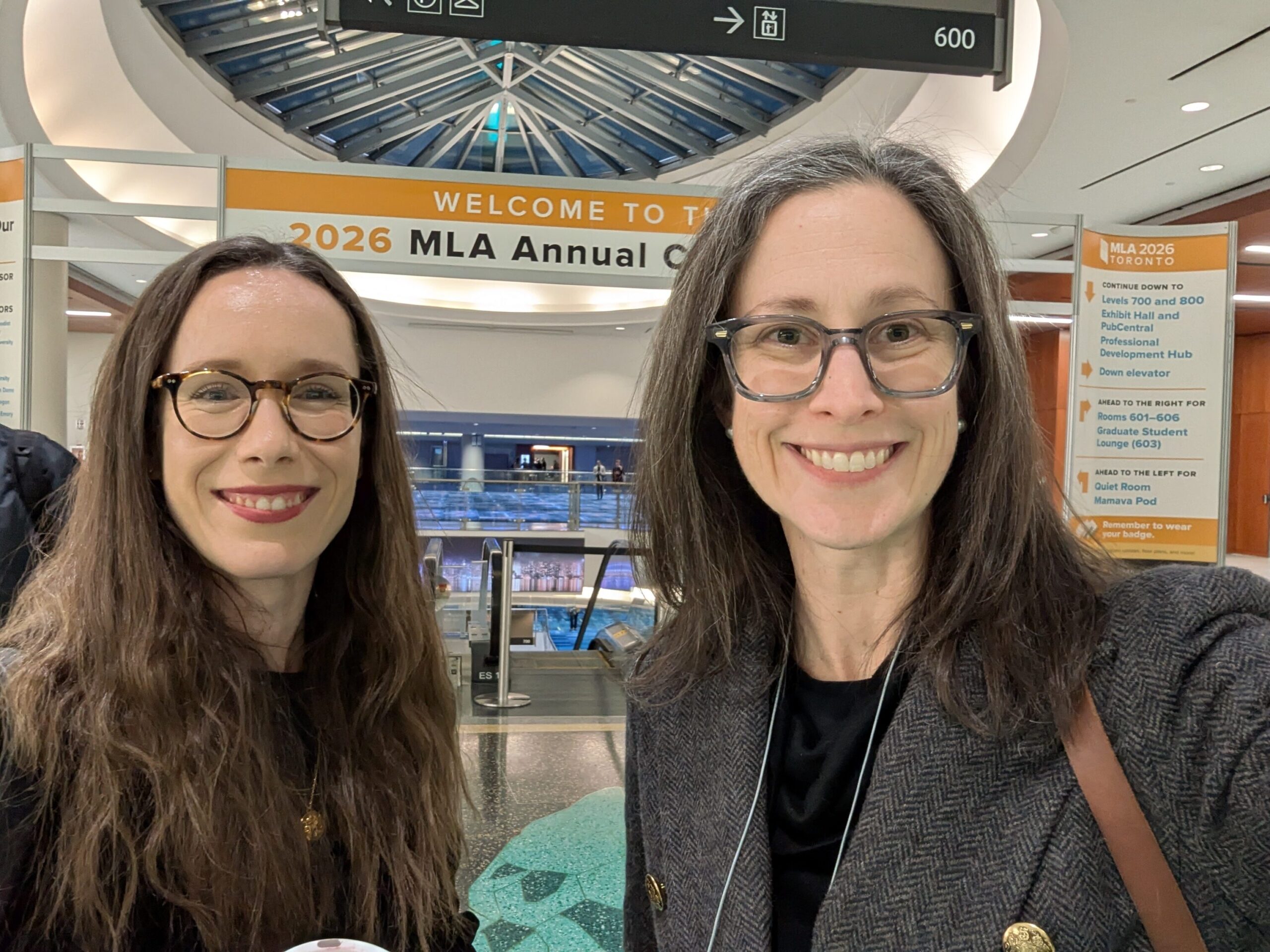 Two women stand smiling in front of the 2026 MLA Convention banner
